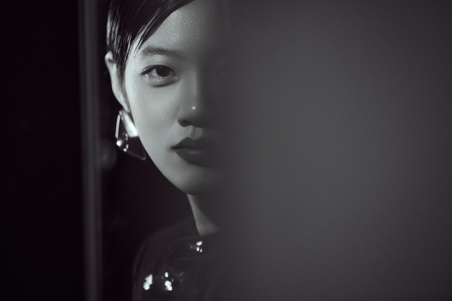 A black-and-white close-up portrait with one eye in clear light and a soft foreground blur, photographed by Hill Xue
