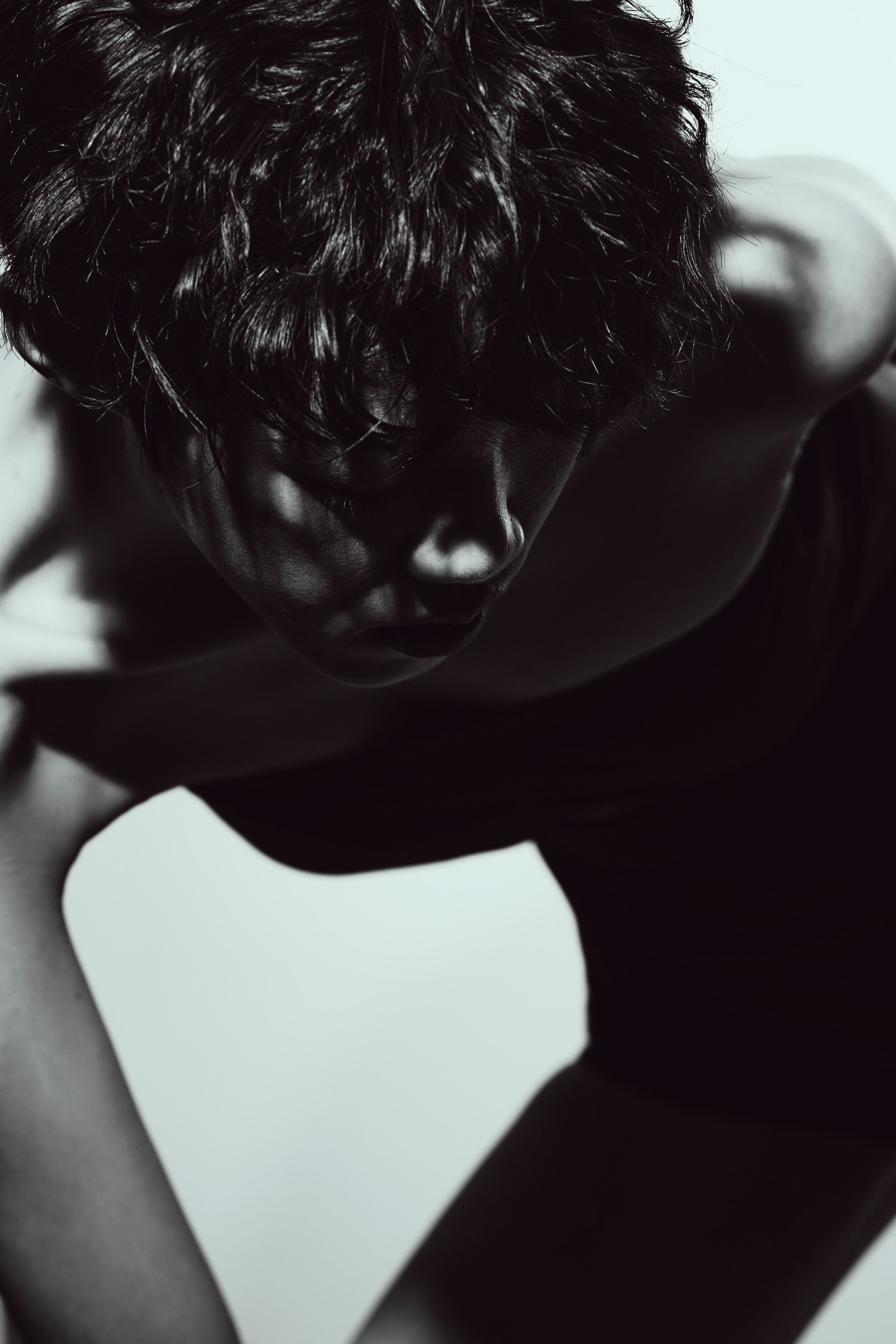 A black-and-white close-up portrait with curly hair and strong directional light, photographed by Hill Xue
