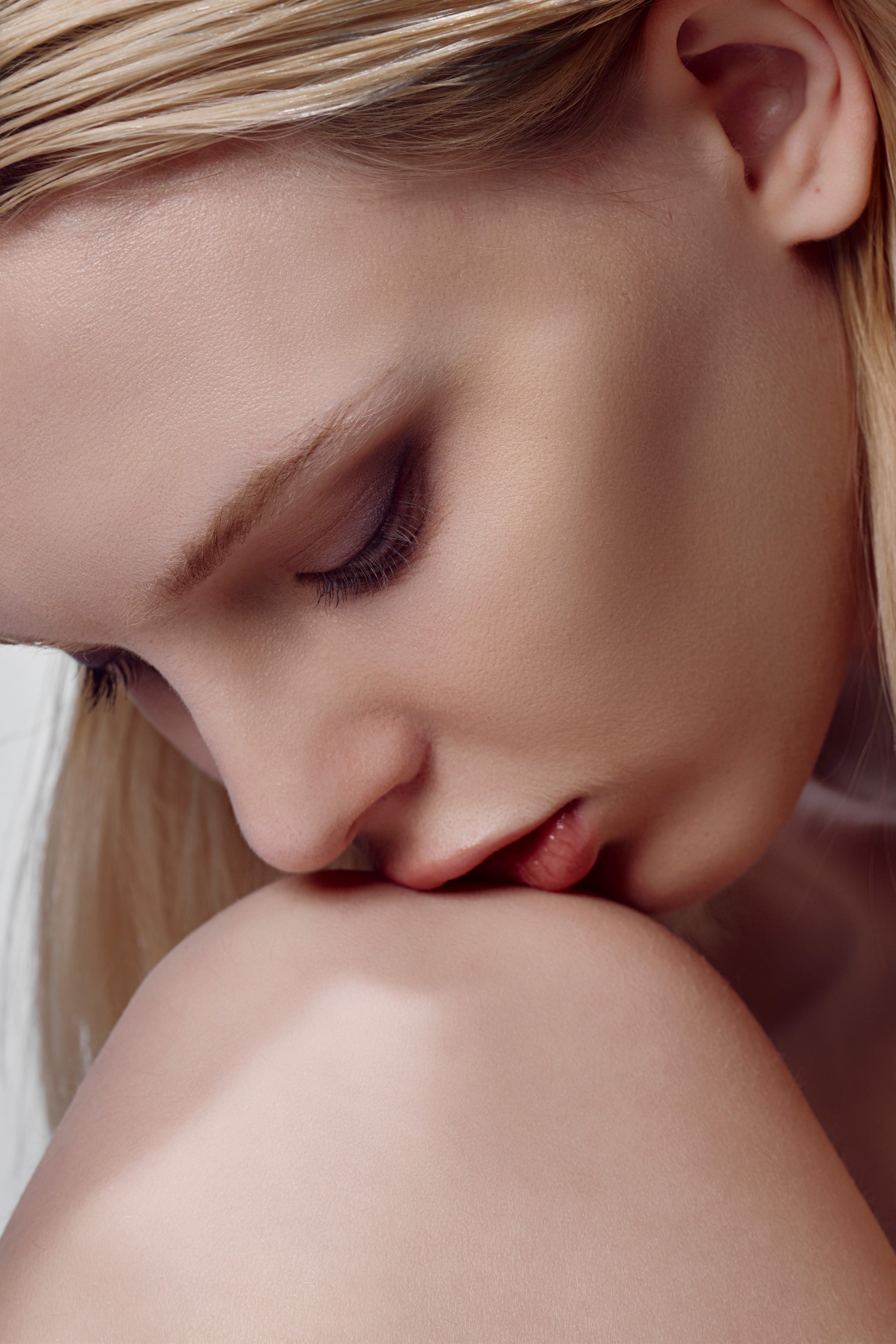 A softly lit color portrait with closed eyes and the face resting against a shoulder, photographed by Hill Xue